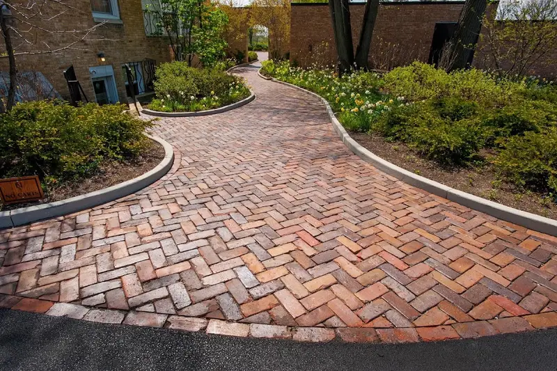 A curving herringbone brick paver walkway edged with flower beds