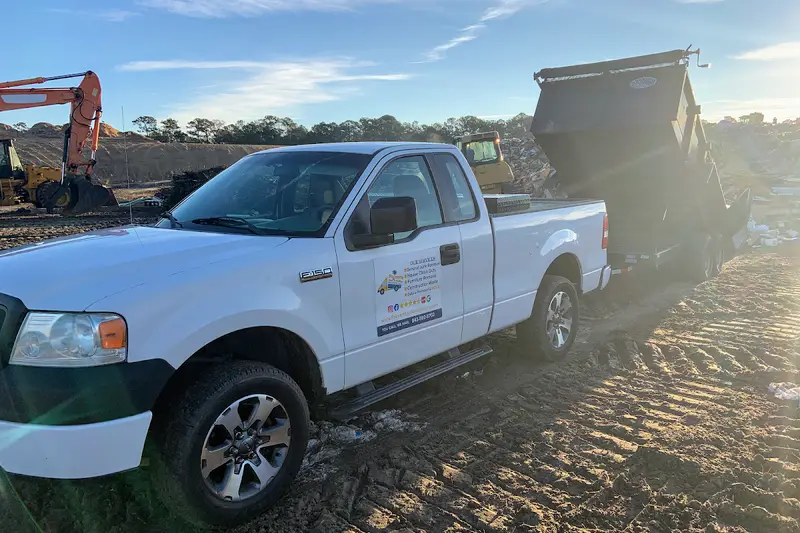 A pickup truck with a dump trailer unloading junk at a landfill