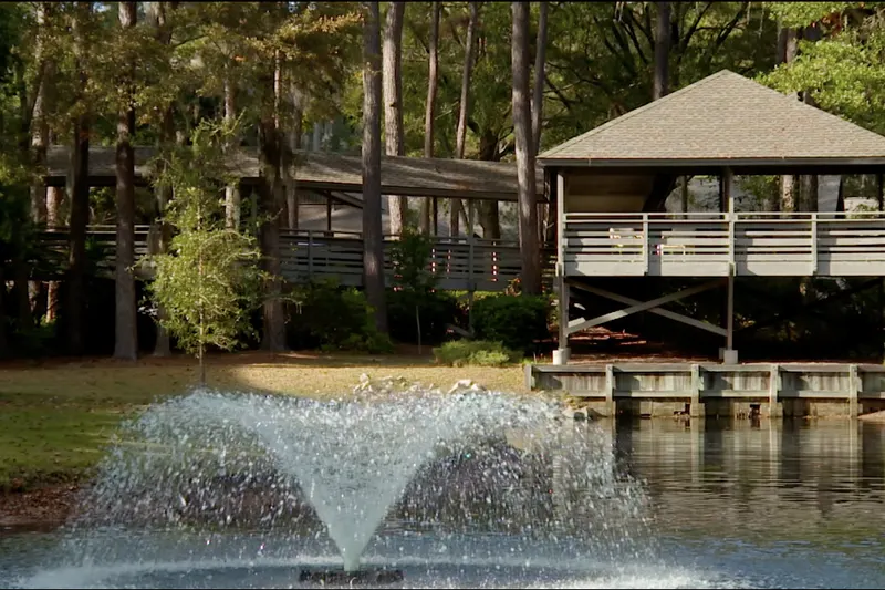 A fountain in the pond at The Seabrook with a gazebo and wooded grounds behind