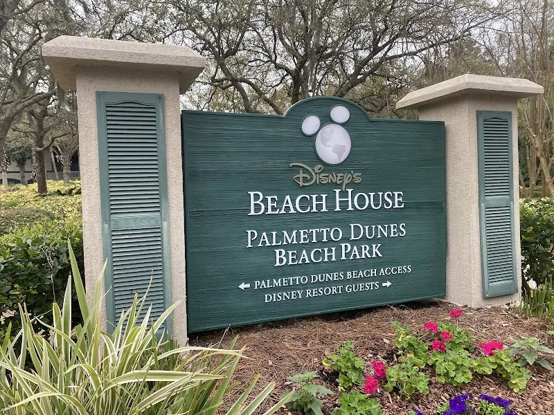 The Disney’s Beach House sign at the Palmetto Dunes beach entrance, among palmettos and flowers