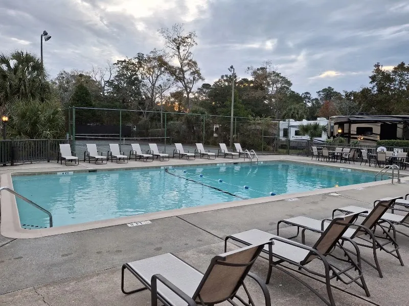 The pool at Hilton Head Harbor RV Resort with lounge chairs and RVs parked beyond the fence
