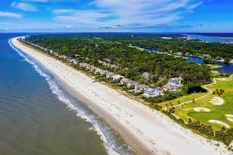 Aerial view of the Palmetto Dunes beach, a long stretch of white sand with houses, lagoons and a golf course behind the dunes