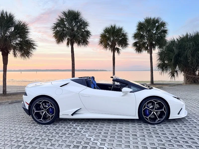 A white Lamborghini convertible parked on a brick-paver lot in front of palm trees at sunset on Hilton Head Island