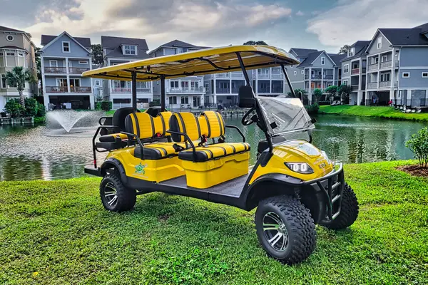 A yellow six-seat Sea Turtle Rentals LSV on the grass by a lagoon and beach houses