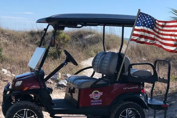 A red Wheelz of Hilton Head golf cart parked on a beach path in the dunes