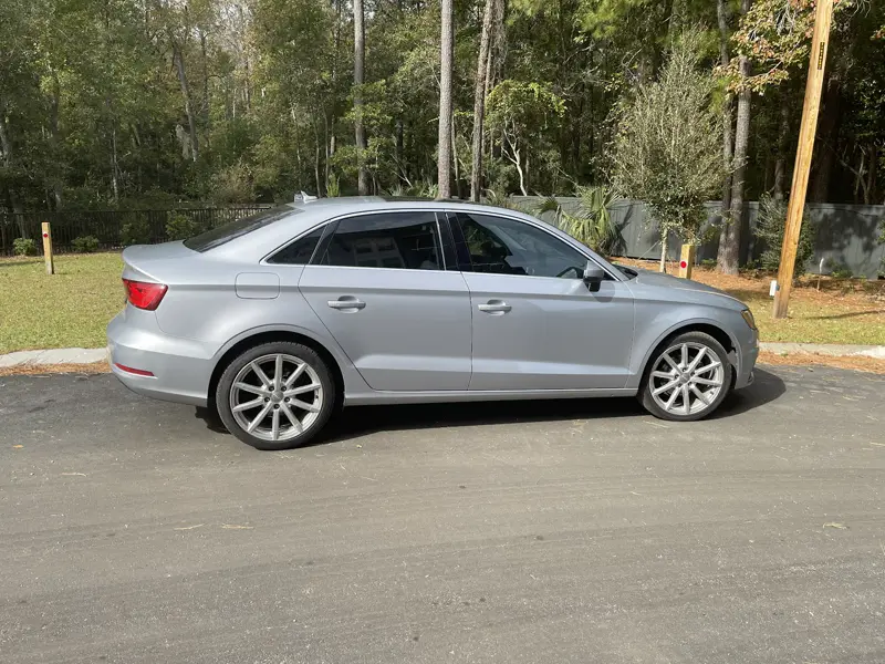 A silver sedan used for M&J Ridez airport rides, parked by the trees
