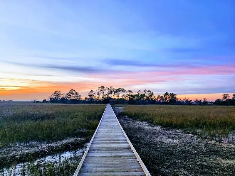 A narrow wooden boardwalk running out over the salt marsh at Hunting Island at sunset
