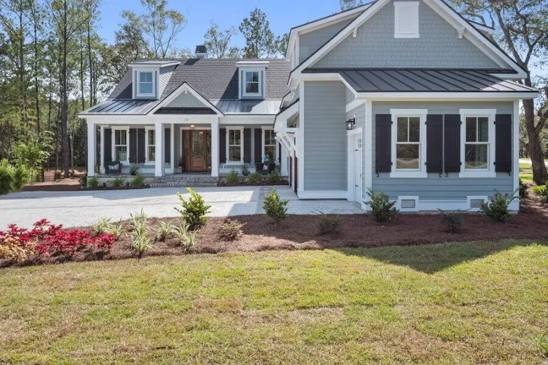 A gray-blue two-story house with a front porch and red flowers along the lawn