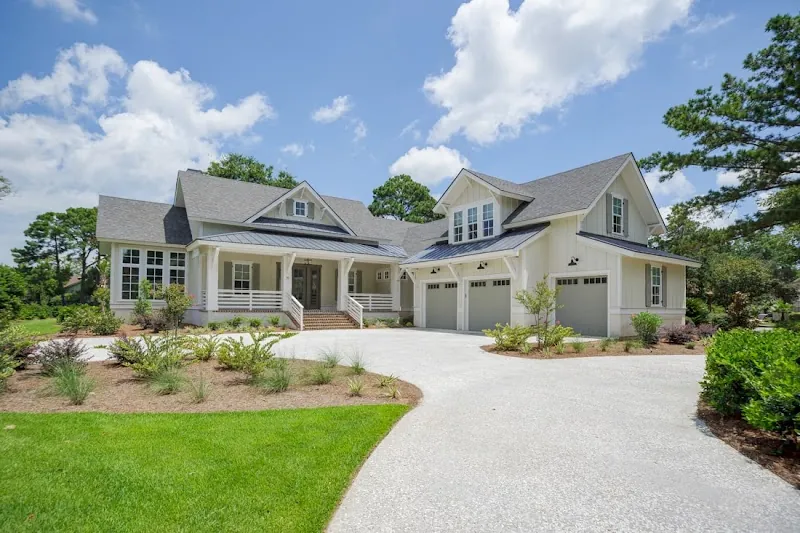 A cream Lowcountry house with dormers and a three-car garage at the end of a curved drive