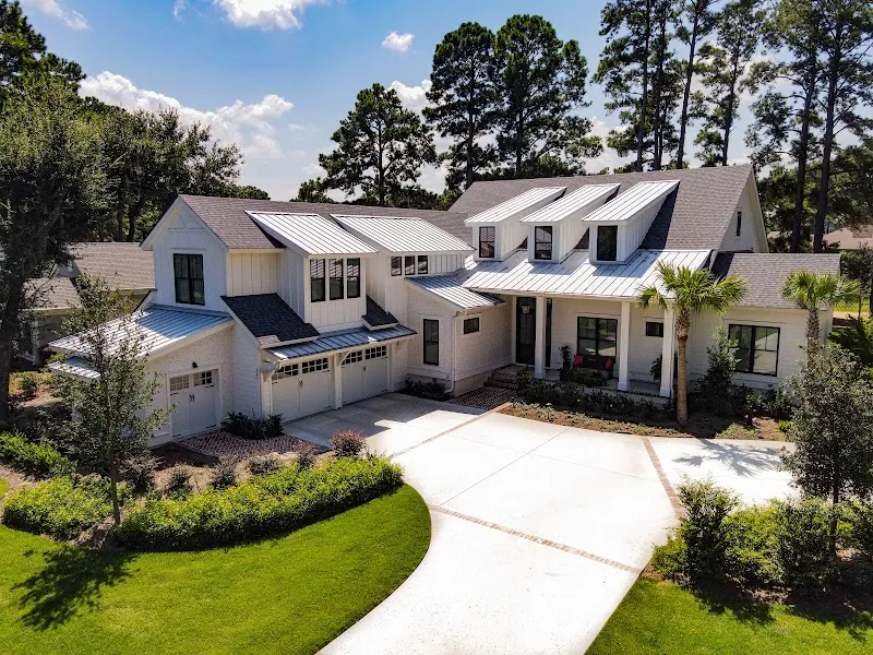 A white house with dormers and a two-car garage behind a new lawn and palms