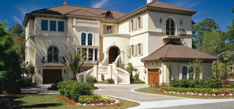 A three-story Mediterranean-style house with a tile roof behind a circular drive