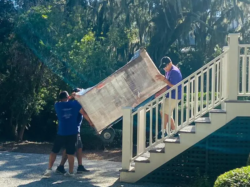 Two movers carrying a table up the outdoor stairs of a raised Hilton Head house