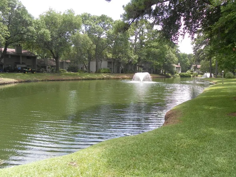 A lagoon with a fountain and condo buildings among live oaks at Woodlake Villas on Mathews Drive
