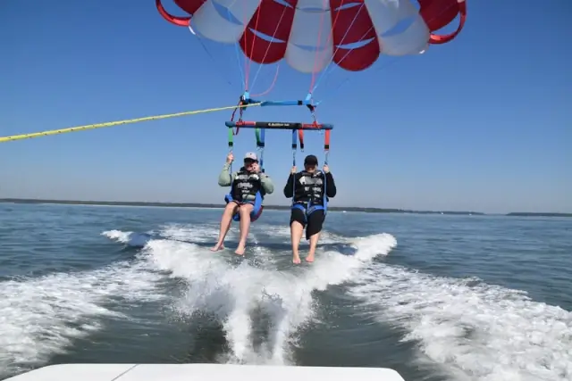 Two parasailers lifting off the wake of a boat on Calibogue Sound under a red-and-white canopy