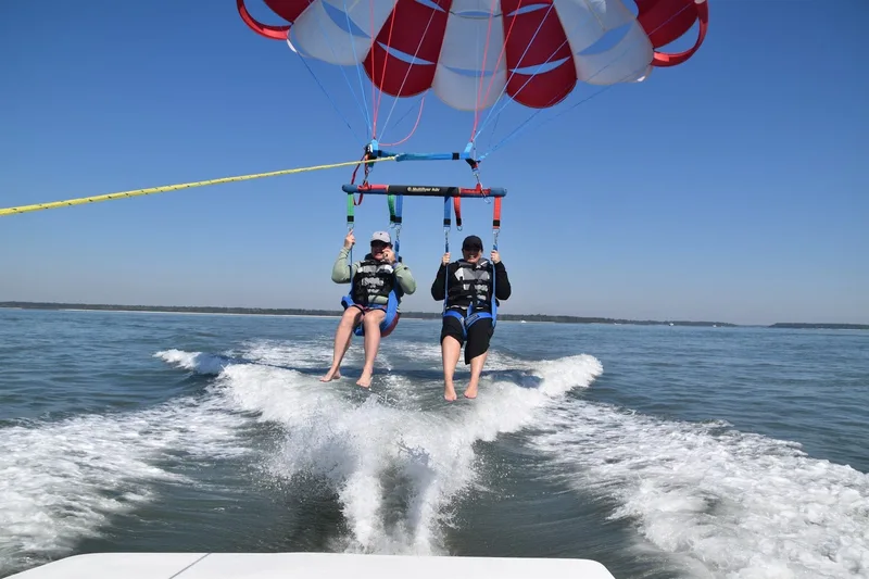Two parasailers lifting off the wake of a boat on Calibogue Sound under a red-and-white canopy
