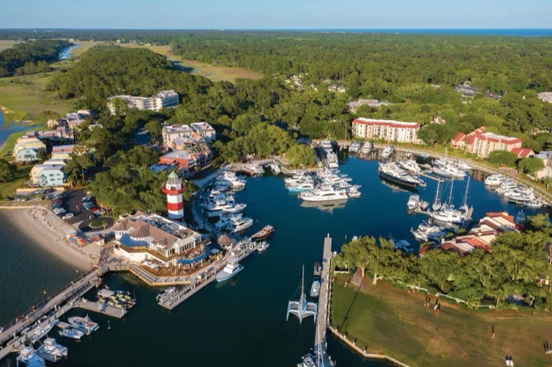 An aerial view of the Harbour Town Yacht Basin, the red-and-white lighthouse, and boats docked around the harbor