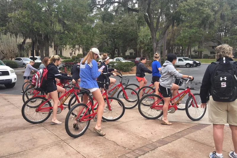 A group collecting red Pelican Cruiser rental bikes under live oaks on Hilton Head