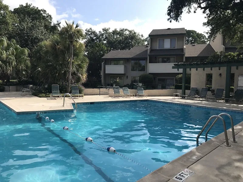 The pool at Stoney Creek Villas with lounge chairs and a villa building under live oaks
