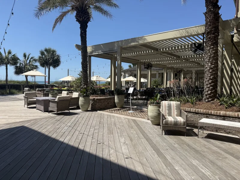 The deck at Coast in the Sea Pines Beach Club, with lounge chairs, umbrellas and the ocean past the palms