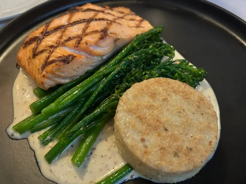 Grilled salmon with broccolini and a grit cake in a cream sauce, a dinner plate at CQ’s in Harbour Town