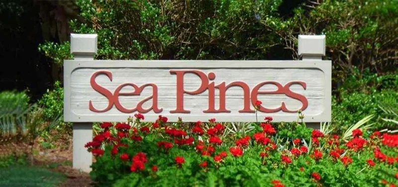 The wooden "Sea Pines" entrance sign, surrounded by red flowers and greenery