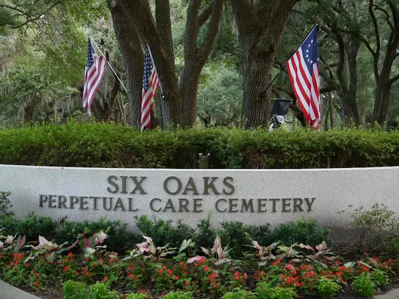 The Six Oaks Perpetual Care Cemetery entrance sign under live oaks and flags in Sea Pines
