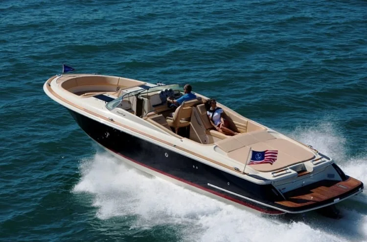 A navy-hulled Chris Craft launch with tan upholstery under way on open water