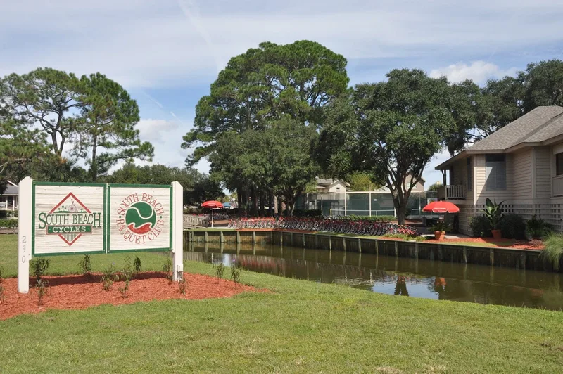 The South Beach Cycles sign at 230 South Sea Pines Drive with a long rack of red rental cruisers beside the lagoon
