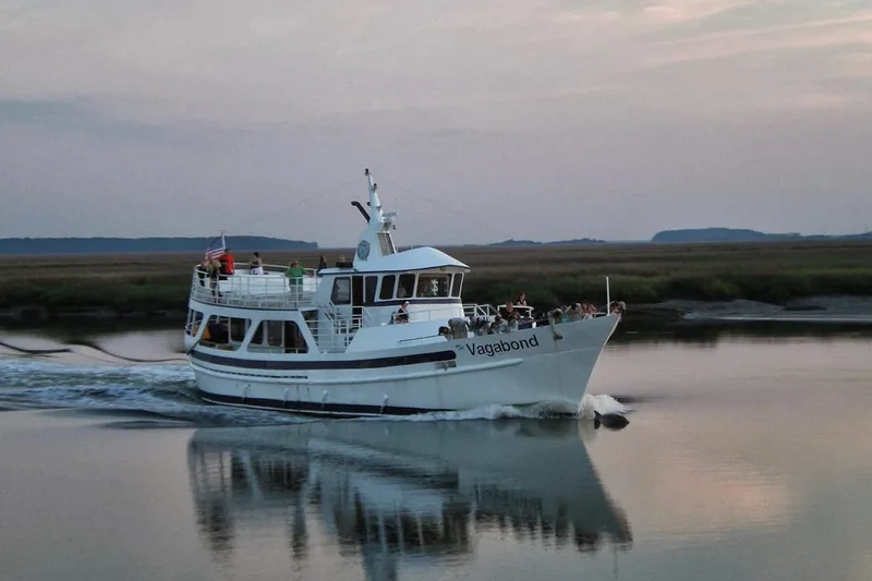 The sightseeing boat Vagabond under way past the marsh at dusk, her name painted on the bow