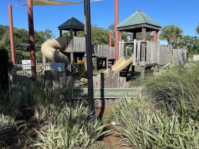 The wooden play structure at Shelter Cove Community Park, with slides and two towers, behind the park’s sign