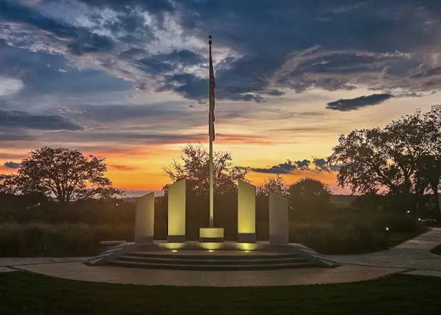 The Shelter Cove Veterans Memorial at sunset: four granite columns around a flagpole, lit from below