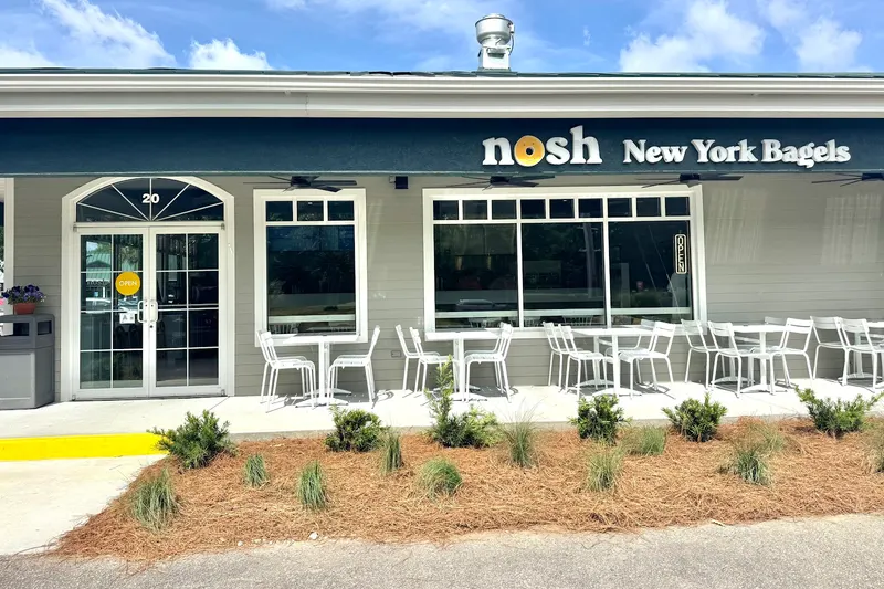 The storefront of Nosh New York Bagels in Ridgeland, with white tables and chairs on the sidewalk