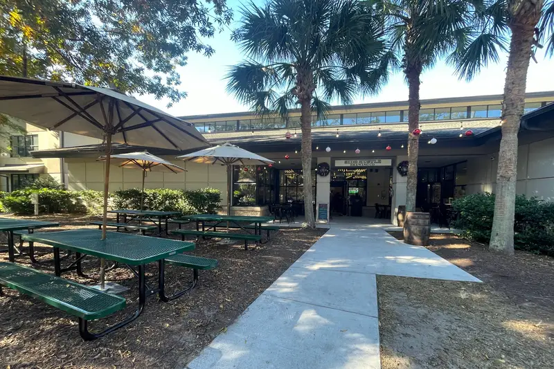 Picnic tables and umbrellas in the palm-shaded beer garden in front of Side Hustle Brewing in Bluffton