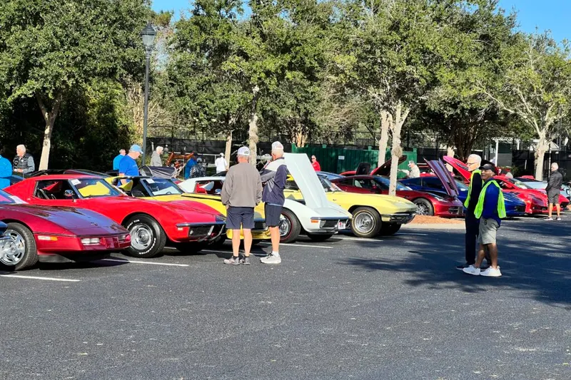 Corvettes and classic cars with their hoods up and residents looking on at the Sun City Car Show outside Magnolia Hall