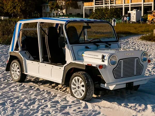 A white electric Moke with a striped bimini top parked on the sand