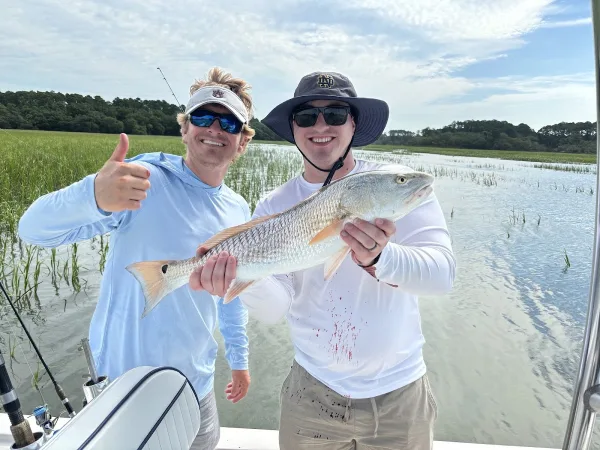 Two anglers holding a redfish in the marsh with Out of the Blue Fishing Charters