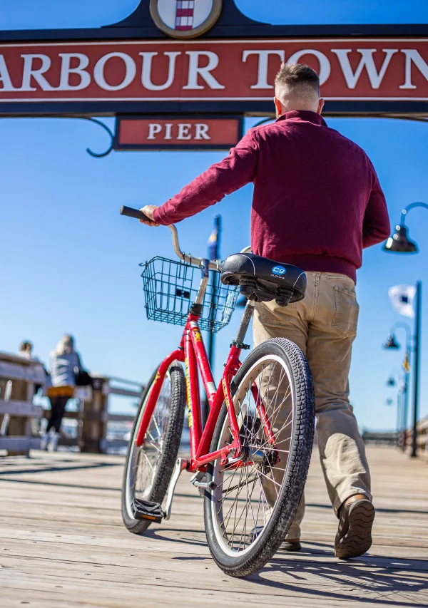 A rider with a red Peddling Pelican bike by the Harbour Town pier sign