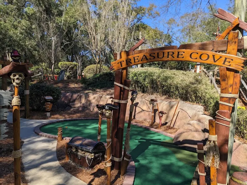 The wooden Treasure Cove arch over a green with a treasure chest, at Pirate’s Island Adventure Golf