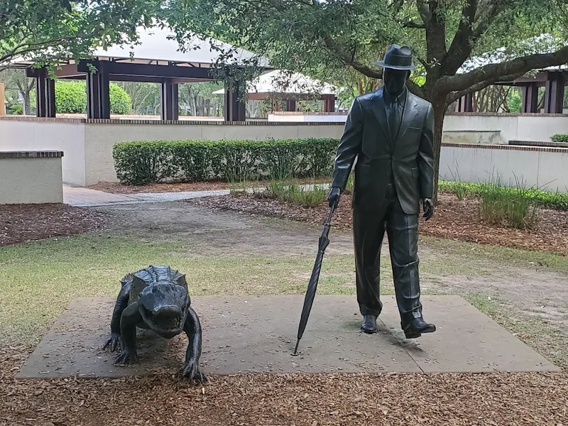 A bronze statue of a man in a hat with an umbrella walking beside a bronze alligator in Compass Rose Park
