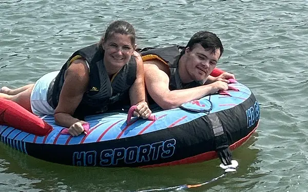Two smiling riders in life jackets lying on a tube on calm creek water
