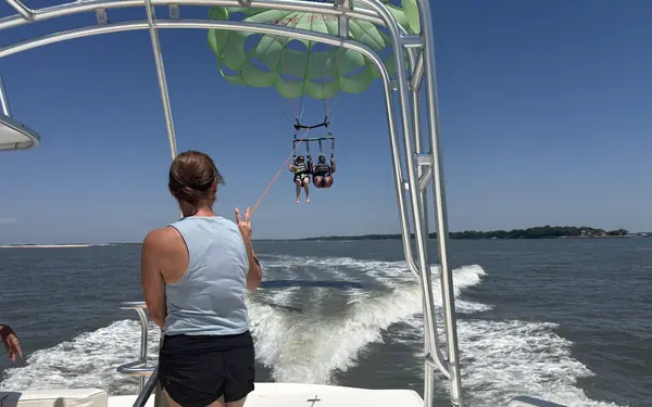 A guest watching two riders under a green parasail from the back of a Sky Pirate boat on Broad Creek