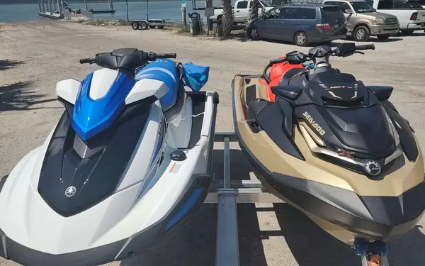 Two jet skis, one blue and white and one tan and black, side by side on a trailer
