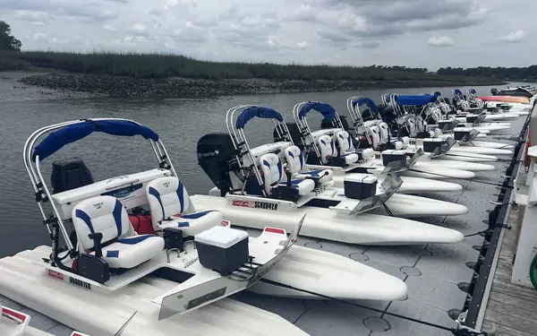 A row of small self-drive mini boats with blue canopies tied up along a floating dock on the marsh