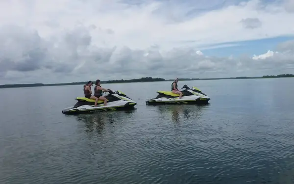 Riders on two jet skis idling on wide, calm water under a cloudy sky