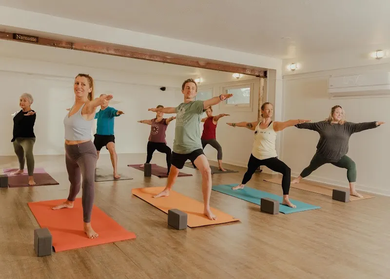 A yoga class in warrior pose on colored mats in the bright Jiva Yoga Center studio