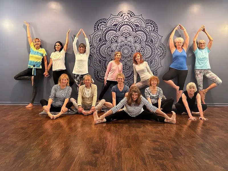 A group of students posing in wide-legged stretches in front of a mandala mural at The Yoga & Pilates Co-Op