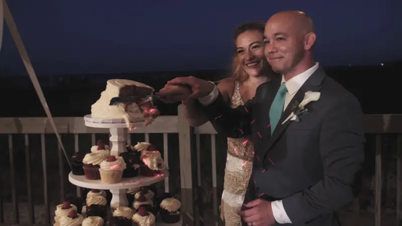 A couple cutting their wedding cake on a deck above a Hilton Head beach at dusk