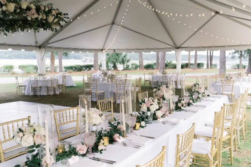 Reception tables under a white tent on a waterfront lawn, set by Simply Southern Events